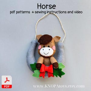 Può includere: Un ornamento a forma di cavallo in feltro con un ferro di cavallo, un fiocco rosso e foglie verdi. Il cavallo ha un corpo marrone, un cappello marrone scuro e guance rosa. Il testo "Horse" e "pdf patterns + sewing instructions and video" sono in alto.
