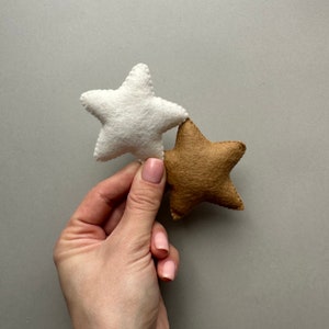 May include: Two felt stars, one white and one brown, are held in a hand. The stars are sewn together.