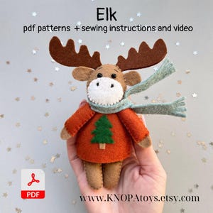 May include: A handmade felt elk doll with brown antlers, a light brown face, and a green Christmas tree on its orange sweater. The elk wears a light blue scarf. Text on the image reads "Elk pdf patterns + sewing instructions and video."