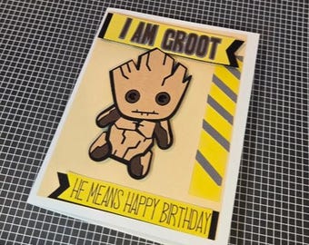 Puede incluir: Una tarjeta de felicitación rectangular con una ilustración de dibujos animados de una criatura marrón similar a un árbol. La tarjeta incluye el texto I AM GROOT arriba y HE MEANS HAPPY BIRTHDAY abajo, con rayas diagonales amarillas y negras.