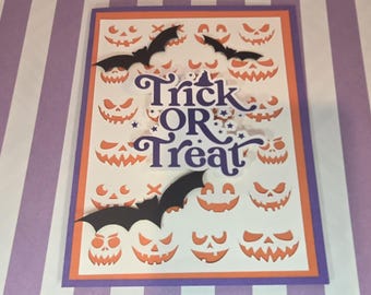 Puede incluir: Una tarjeta de felicitación rectangular con fondo blanco y un patrón repetitivo de caras de calabaza naranjas. La tarjeta tiene bordes morados y naranjas, tres murciélagos de papel negros y el texto morado Trick OR Treat.