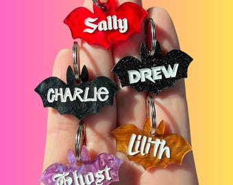 Peut inclure: Cinq porte-clés en forme de chauve-souris avec des paillettes et de différentes couleurs. Les porte-clés sont personnalisés avec les noms "Sally", "Drew", "Charlie", "Lilith" et "Ghost".
