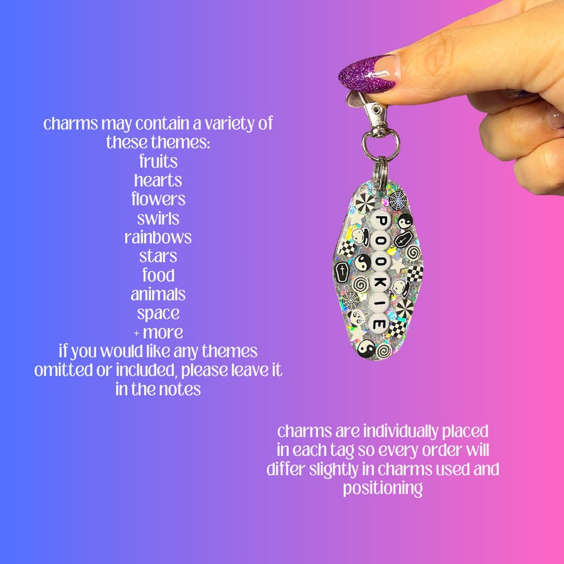 May include: A silver charm keychain with a clear resin tag that says "POOKIE" in white letters. The tag is filled with colorful and black and white charms, including hearts, stars, and swirls.
