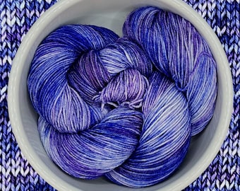 Könnte beinhalten: Eine Schüssel mit lila und blauem Garn mit weißen Streifen. Das Garn ist weich und flauschig und perfekt zum Stricken oder Häkeln.
