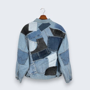 May include: A denim jacket with a patchwork design. The jacket features various shades of blue denim patches, including light, medium, and dark washes, creating a unique and textured appearance. The jacket is hanging on a wooden hanger.