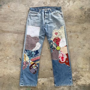 Può includere: Jeans in denim azzurro con elaborati disegni patchwork su entrambe le gambe. Le toppe sono composte da vari motivi di tessuto, tra cui trame floreali, a righe e a tinta unita, disposte in grandi forme di fiori con una faccina gialla sorridente.