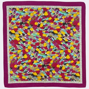 Puede incluir: Pañuelo cuadrado con un estampado floral en tonos rojos, amarillos, morados y azules. El pañuelo tiene un borde magenta oscuro con el nombre de la marca en blanco. Un accesorio elegante.