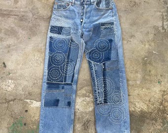 Calça jeans vintage Levi's 501 feita sob encomenda, com detalhes em denim repaginado, costura sashiko e patchwork reciclado. Peça única e exclusiva.
