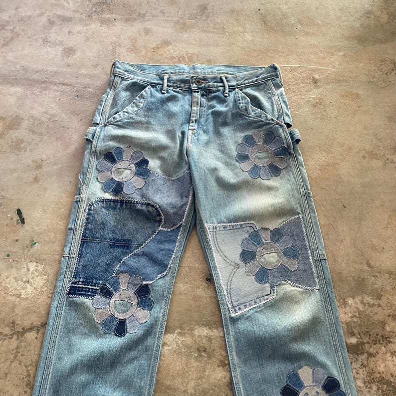May include: Light blue denim jeans with multiple patches and flower appliqu&eacute;s. The jeans feature a classic five-pocket design and a straight leg cut. Patches and flower appliqu&eacute;s are in shades of blue.