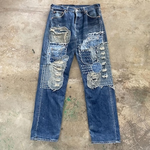 Könnte beinhalten: Blaue Jeans mit sichtbaren Patches und Used-Details. Die Patches sind mit sichtbaren Nähten auf die Jeans genäht. Die Jeans hat einen Knopfverschluss und ein klassisches Fünf-Taschen-Design. Die Jeans hat eine mittlere Waschung.