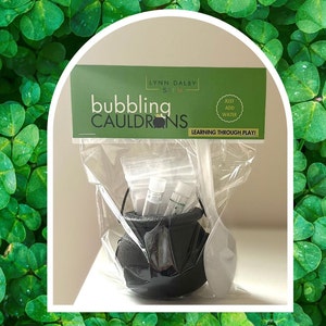 May include: A black cauldron with a white spoon and clear plastic bags containing bubbling cauldron science experiment supplies. The packaging has the text "Bubbling Cauldrons" and "Learning Through Play!"