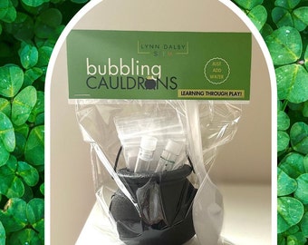 May include: A black cauldron with a white spoon and clear plastic bags containing bubbling cauldron science experiment supplies. The packaging has the text "Bubbling Cauldrons" and "Learning Through Play!"