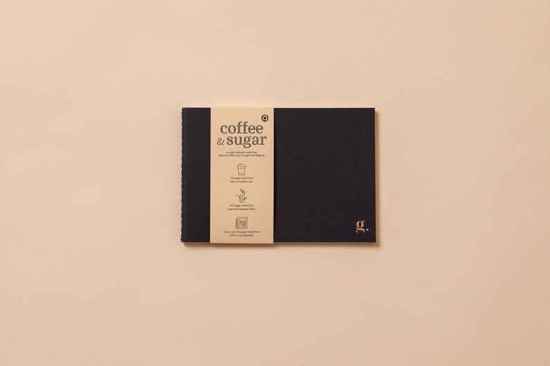 May include: A black notebook with a brown paper cover that says "coffee & sugar" and has a small illustration of a coffee cup. The notebook has a gold "J.G." logo on the front cover.