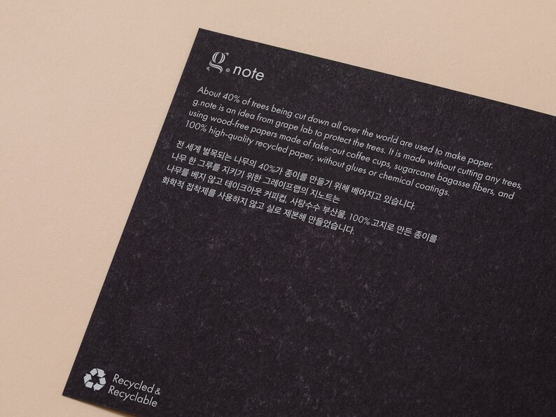 May include: A black and white image with the text "g.note" in white. The text explains that the paper is made from recycled materials, including coffee cups, sugarcane bagasse fibers, and recycled paper. The text also states that the paper is made without cutting down any trees. The image also includes a recycling symbol with the text "Recycled & Recyclable" in white.