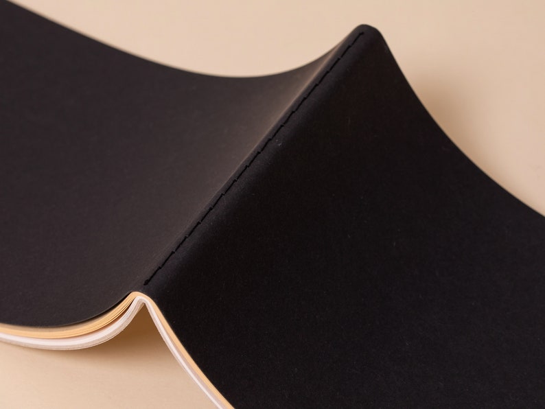 May include: A black notebook with a stitched spine and a cream colored edge.