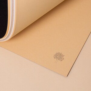 May include: A close-up of a light brown paper with a simple line drawing of a tree in the center. The paper is folded over on itself, revealing a black and white striped pattern underneath.
