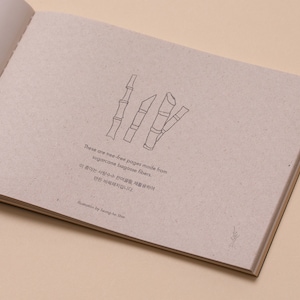 May include: Close-up of a page from a book made from sugarcane bagasse fibers. The page is textured and has a drawing of sugarcane stalks. The text reads: "These are tree-free pages made from sugarcane bagasse fibers. 이 종이는 사탕수수 섬유질을 재활용하여 만든  목재지입니다."