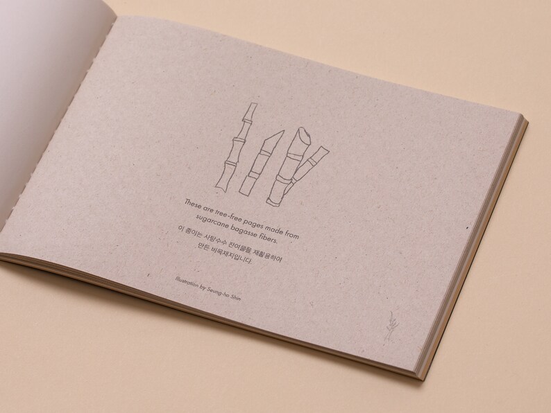 May include: Close-up of a page from a book made from sugarcane bagasse fibers. The page is textured and has a drawing of sugarcane stalks. The text reads: "These are tree-free pages made from sugarcane bagasse fibers. 이 종이는 사탕수수 섬유질을 재활용하여 만든  목재지입니다."