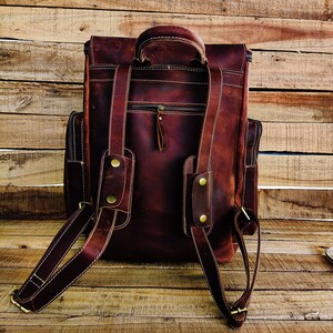 May include: A brown leather backpack with adjustable straps and a zippered front pocket. The backpack has a top handle and brass hardware.