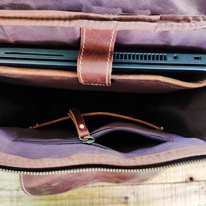 May include: A brown leather backpack with a zippered pocket and a flap that opens to reveal a padded laptop compartment. The laptop compartment is lined with a soft, dark fabric.