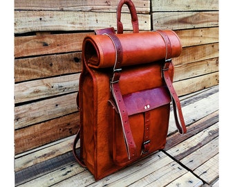 Könnte beinhalten: Ein brauner Lederrucksack mit Rollverschluss und verstellbaren Trägern. Der Rucksack hat ein großes Frontfach mit einer Schnallenverschluss.