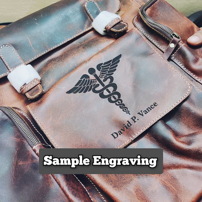 May include: A brown leather backpack with a zippered pocket on the front. The pocket has a black engraved medical symbol and the text "David P. Vance".