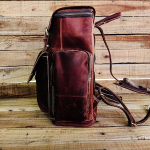 May include: A brown leather backpack with a zippered top closure and adjustable straps. The backpack has a large main compartment and a smaller front pocket.