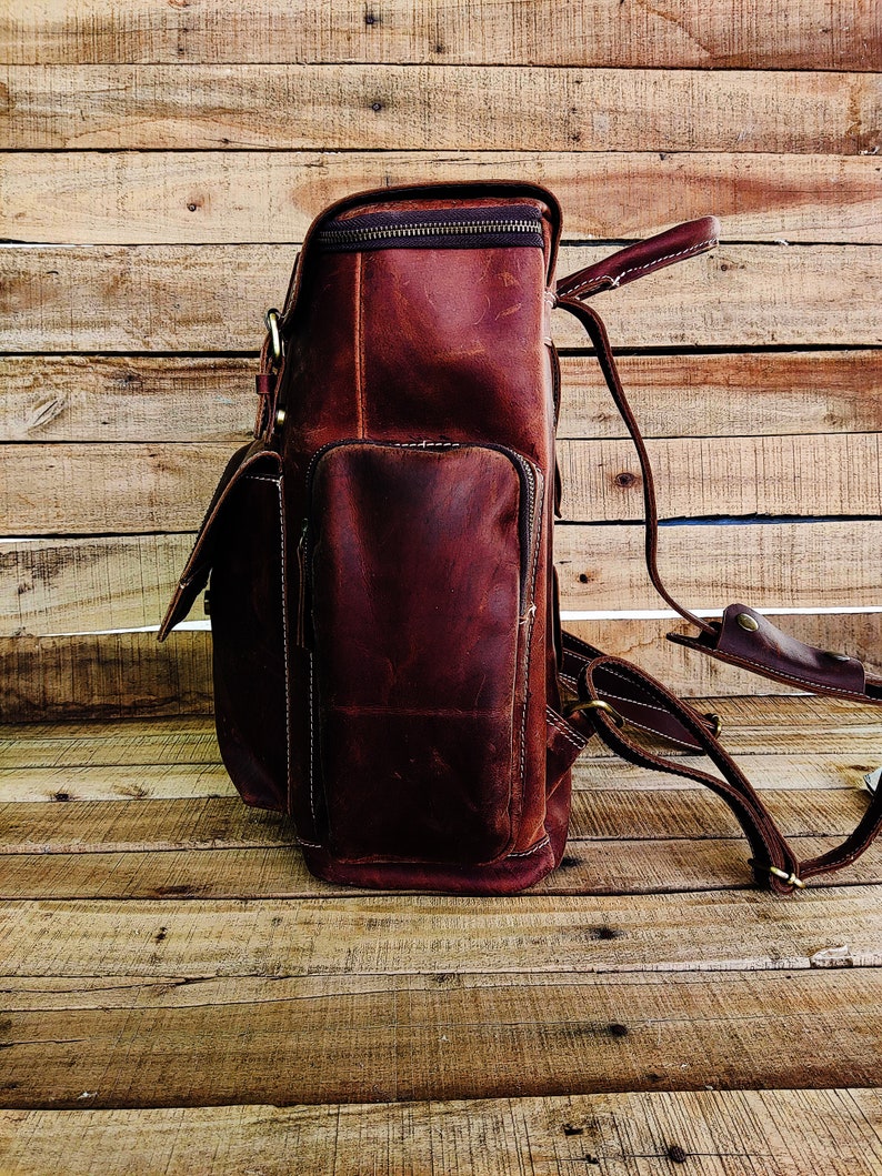 May include: A brown leather backpack with a zippered top closure and adjustable straps. The backpack has a large main compartment and a smaller front pocket.