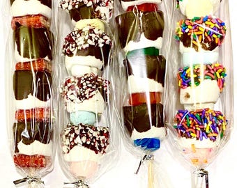 May include: Four chocolate-covered marshmallow skewers with different toppings. The skewers are wrapped in clear plastic and tied with silver ribbon. The toppings include red and white sprinkles, colorful sprinkles, and a red and white candy.