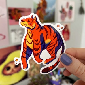 May include: A sticker of an orange and purple tiger with a white background. The tiger is standing on its hind legs with its head tilted up. There are small yellow stars around the tiger.