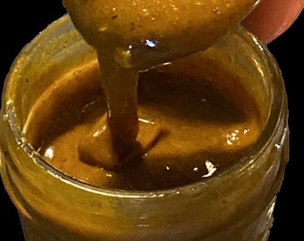 Könnte beinhalten: Nahaufnahme eines Glasbehälters gefüllt mit einer dicken, goldbraunen Sauce. Die Sauce wird mit einem Löffel entnommen, wodurch ihre glatte und cremige Textur sichtbar wird.