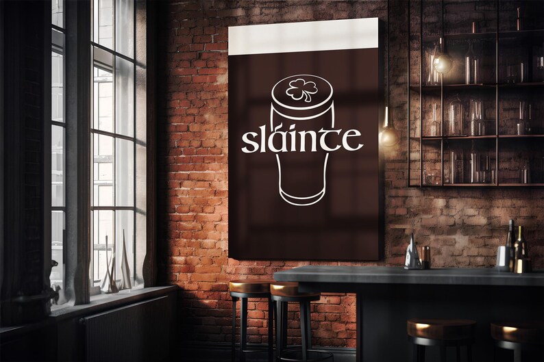 K&ouml;nnte beinhalten: Ein dunkelbraunes Schild mit dem Wort "sl&aacute;inte" in wei&szlig;er Schrift, &uuml;ber einer wei&szlig;en Umrisszeichnung eines Bierglases mit einem Kleeblatt. Das Schild h&auml;ngt an einer Backsteinmauer in einer Bar.