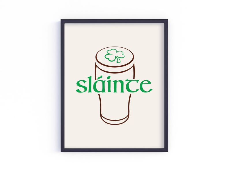 K&ouml;nnte beinhalten: Gerahmter Kunstdruck mit einer braunen Umrisszeichnung eines Bierkrugs und einem gr&uuml;nen Kleeblatt. Das Wort "sl&aacute;inte" steht in gr&uuml;ner Schrift darunter. Der Hintergrund ist hellbeige.