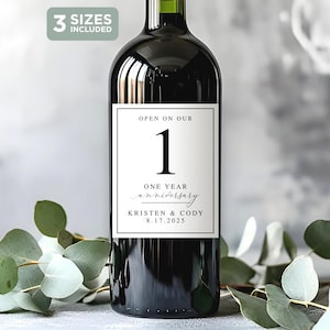 May include: A dark wine bottle with a white label that reads "OPEN ON OUR 1 ONE YEAR anniversary" with the names Kristen & Cody and the date 8.17.2025. The image includes eucalyptus leaves and the text "3 SIZES INCLUDED".