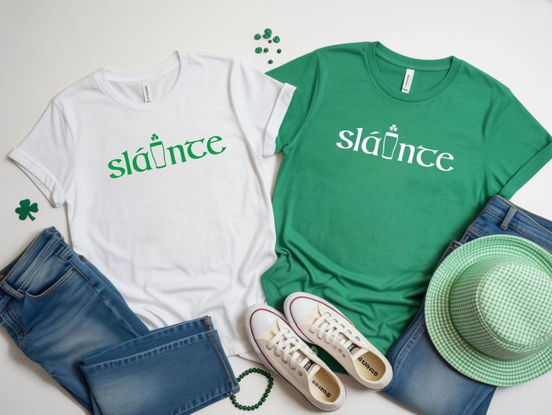 Puede incluir: Dos camisetas, una blanca y otra verde, con la palabra "sl&aacute;inte" en verde y blanco, respectivamente. La palabra va acompa&ntilde;ada de un gr&aacute;fico de una pinta y un tr&eacute;bol. Las camisetas se combinan con vaqueros, zapatos y un sombrero.
