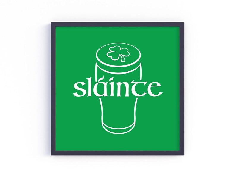 K&ouml;nnte beinhalten: Quadratischer gerahmter Druck mit gr&uuml;nem Hintergrund, der eine wei&szlig;e Umrisszeichnung eines Bierkrugs mit einem Kleeblatt oben zeigt. Das Wort "sl&aacute;inte" ist in wei&szlig;er Schrift auf der Vorderseite des Bierkrugs geschrieben.