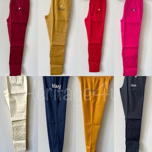 May include: Eight pairs of cotton pants in various colors, including burgundy, beige, red, pink, off-white, navy, mustard, and black. Each pair has a small embroidered label with the color name.
