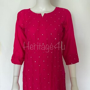 May include: A pink, long-sleeved, embroidered top with a V-neckline and a diamond pattern. The top is decorated with small, round, reflective sequins.