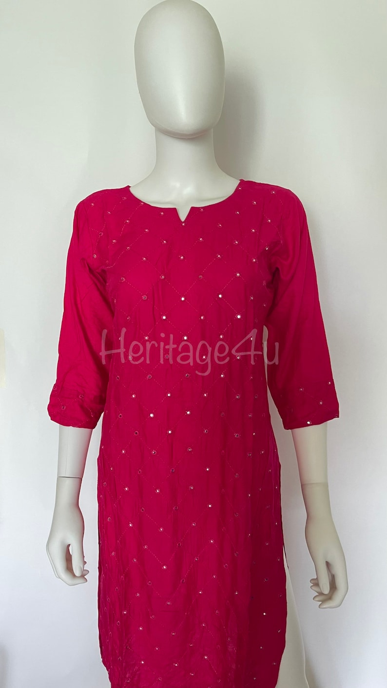 May include: A pink, long-sleeved, embroidered top with a V-neckline and a diamond pattern. The top is decorated with small, round, reflective sequins.
