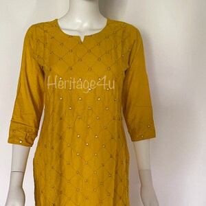 May include: A mustard yellow kurta with a diamond pattern and gold embellishments. The kurta has a round neckline and three-quarter sleeves.