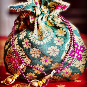 Peut inclure: Un sac à cordon vert avec des broderies florales dorées et roses. Le sac a un long cordon rose avec des glands dorés.