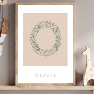 May include: A framed print featuring a floral design in the shape of the letter "O" on a pale pink background. The name "OLIVIA" is printed beneath the design.