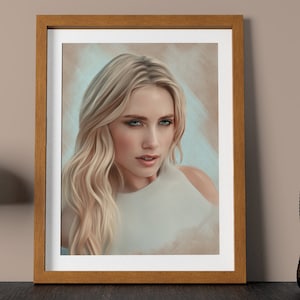 May include: A framed portrait of a woman with long, wavy blonde hair and blue eyes. The artwork is in a wooden frame and is displayed on a dark surface. A gold-colored lamp and a decorative glass vase are also visible.