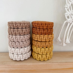 May include: A stack of six beige crocheted coasters and a stack of six brown and yellow crocheted coasters. The coasters are round and have a woven texture.