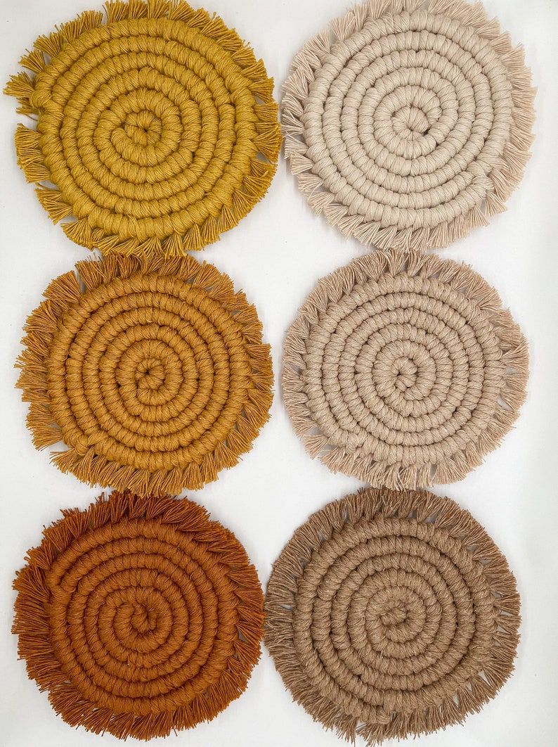 May include: Six round crocheted coasters with fringe. The coasters are in shades of brown, beige, and yellow.