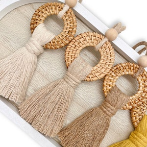 May include: Three woven rattan hoops with tassels. The tassels are in beige, brown, and yellow.