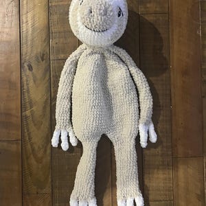 May include: A handmade, plush sloth doll in a light beige colour with a white head and white accents on the hands and feet. The sloth has a smiling face with small black eyes. The doll is made of a soft, textured material.