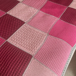 May include: A pink and red crocheted blanket with a variety of stitch patterns. The blanket is made up of squares with different textures.