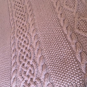 May include: A close-up of a knitted blanket with a cable knit pattern in a dusty rose colour.