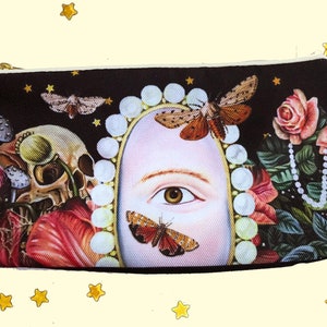 Op de afbeelding: Een zwarte canvas ritszak met een kleurrijke print met een schedel, paddenstoelen, bloemen, vlinders en een enkel oog in een parelversierd frame.